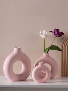 two pink vases sitting on top of a white shelf next to a purple flower