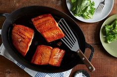 salmon being cooked in a skillet with lettuce and seasoning on the side