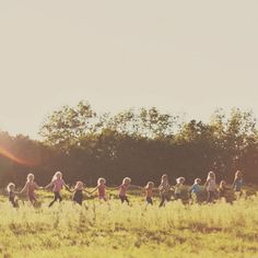 a group of children running through a field with trees in the background