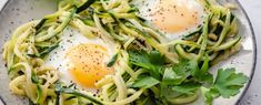 two eggs are on top of some noodles in a white bowl with green garnish