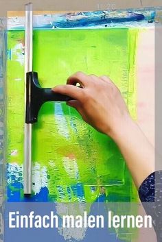 a person is painting on the wall with green and blue paint, while holding a black handle