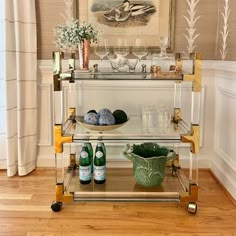 a bar cart with bottles and glasses on it in front of a framed art piece