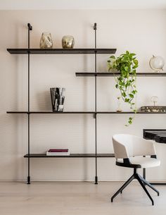 a white chair sitting in front of a black book shelf filled with books and plants