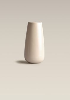 an empty white vase sitting on top of a table next to a gray wall and floor