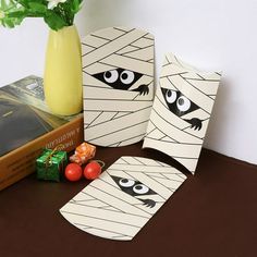 three pieces of paper with eyes on them sitting next to a yellow vase and book