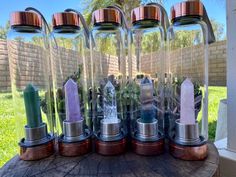 several different types of candles in glass vases on top of a wooden table outside