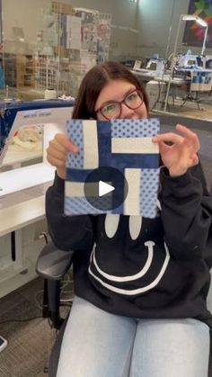 a woman sitting in a chair holding up a piece of blue and white paper with a smiley face on it