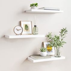 two white floating shelves with plants and pictures on them, one is holding a clock