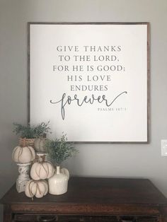 a wooden table topped with white pumpkins next to a framed sign that says give thanks to the lord, for he is god