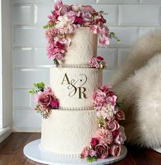 a three tiered wedding cake with pink flowers on the side and monogrammed initials