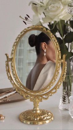 a woman's face is reflected in a gold vanity mirror next to jewelry and flowers