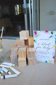 wooden blocks and pens on a table with a card in front of them, next to a vase filled with flowers