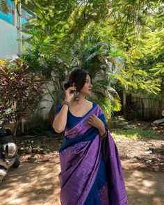 a woman in a blue and purple sari talking on her cell phone while standing outside