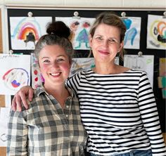 two women standing next to each other in front of pictures on the wall behind them