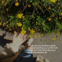 a person sitting on the ground with their hand up in front of them and yellow flowers