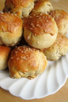 a white plate topped with mini rolls covered in sesame seed toppings on top of a wooden table