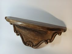 a wooden shelf with carved designs on the top and bottom, against a white wall