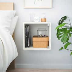 a nightstand with books and plants on it next to a plant in the corner of a room