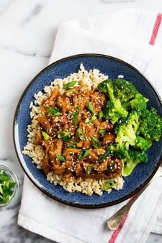 a blue plate topped with rice and broccoli covered in sesame seed chicken sauce