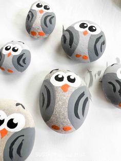 painted rocks with owls on them sitting on a white tablecloth and one has an orange nose