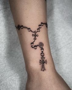 a tattoo on the ankle of a woman with a cross and rosary attached to it