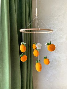 an orange mobile hanging from a curtain with flowers and fruit attached to the strings above it