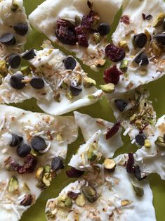 several pieces of fruit and nuts are on a green plate with white frosting, cranberries, pistachios, almonds, and raisins