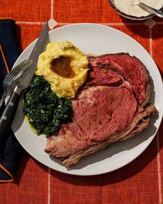 a plate with meat, mashed potatoes and spinach on it next to utensils