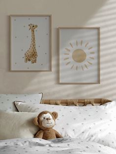 a teddy bear sitting on top of a bed next to two framed giraffes