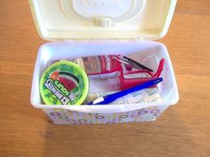 a plastic container filled with different items on top of a wooden table next to a pair of scissors and toothbrushes