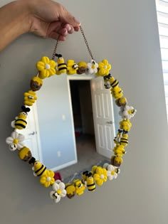 a hand holding a mirror decorated with yellow and black bees on it's chain