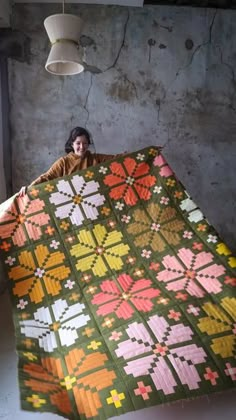 a woman is holding up a large quilt