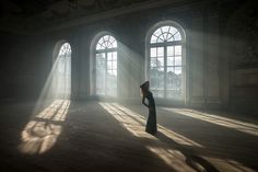 a woman standing in an empty room with sunlight streaming through the windows