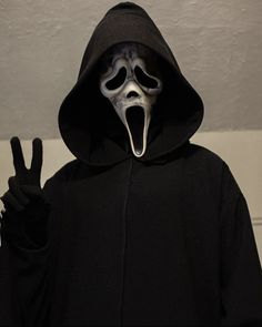 a person wearing a black hooded jacket with a white mask on their face and hands in the air