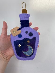 a hand holding up a purple bottle ornament with stars and moon on it