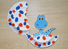 a paper plate with a blue dinosaur on it sitting next to another paper plate that has red and blue dots on it