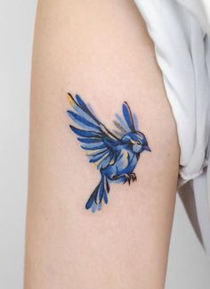 a small blue bird tattoo on the back of a woman's left arm and shoulder