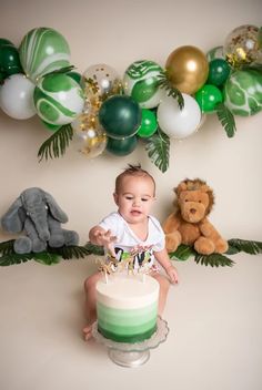 a baby sitting in front of a cake with green and white decorations on the wall