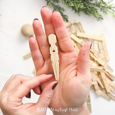 two hands holding small pieces of wood on top of a white surface with greenery