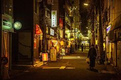 a person walking down an alley way at night with many signs on the side of buildings