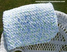 a crocheted blanket sitting on top of a white wicker chair in the grass