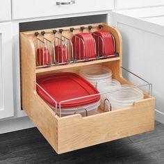 an open drawer in a kitchen filled with red dishes and pans on the counter