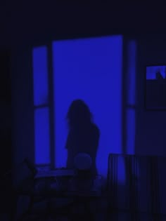 a person standing in front of a window with blue light coming through the windows and their shadow on the table