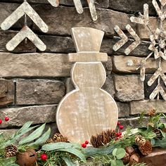 a wooden snowflake sitting in front of a brick wall next to evergreen and pine cones