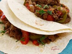 two tacos with meat, peppers and onions on a blue tablecloth next to a fork