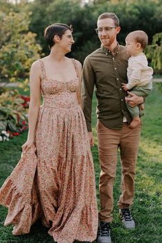 a man and woman are standing in the grass with a baby wearing a dress on