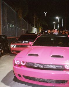 pink cars parked in front of a fence at night with people standing around the car