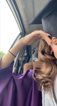 a woman with long hair wearing a graduation cap and gown sitting in the back seat of a car