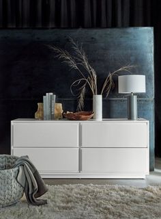 a white dresser sitting on top of a rug next to a lamp and vases