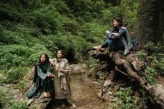 three women are sitting on rocks in the middle of a forest and one is holding a cup